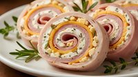 Sliced spiral ham and cheese pinwheels garnished with fresh rosemary on white plate, suitable for appetizers, catering, food photography, and culinary content.