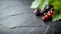 Fresh red currants and blackberries with green leaves on dark slate stone background with copy space. Natural food photography for healthy eating concept.