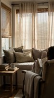 Cozy living room corner with beige sofa, bamboo blinds, linen curtains and wooden side table creating warm neutral interior design atmosphere.