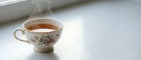 Vintage floral teacup filled with hot tea, steam rising, placed on white surface with natural light for beverage and lifestyle designs.