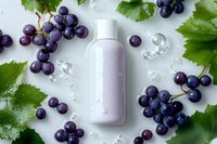 Fresh purple grapes and green leaves frame white cosmetic bottle with water drops on light background, natural skincare concept for beauty product.