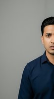 Young South Asian male professional wearing navy blue shirt against neutral gray background, suitable for corporate portraits and business headshots.