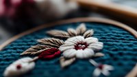 Delicate white flower embroidery on turquoise fabric in wooden hoop, featuring detailed stitching with burgundy accents and wheat stalks, showcasing traditional needlework.