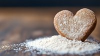 Heart shaped gingerbread cookie dusted with powdered sugar on dark wooden surface, romantic food photography with selective focus and bokeh background.