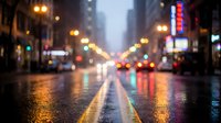 Blurred city street at night with wet asphalt reflecting colorful lights from traffic and neon signs creating atmospheric urban bokeh effect for backgrounds.