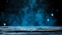Dark wooden table surface against blurred blue bokeh lights and mystical fog background, creating atmospheric mood for product display or creative composition.