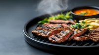 Juicy grilled beef steak sliced on black plate with fresh herbs and sauce. Medium rare meat with golden crust and pink center shows professional cooking technique.