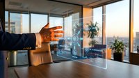 Businessman in dark suit touching transparent digital interface with holographic data visualization and cityscape view from high-rise office window at sunset.
