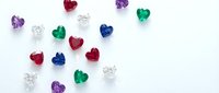 Colorful heart-shaped gemstones scattered on white background. Red, blue, green, purple and clear crystal hearts for jewelry design and romantic themes.