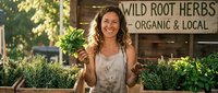 Smiling woman holding fresh herbs at organic farm market stand promoting healthy local produce and sustainable agriculture lifestyle.