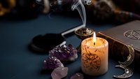 Mystical altar setup with burning candle, amethyst crystals, incense smoke and moon symbols for spiritual rituals and meditation practices.