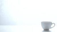 White ceramic coffee cup on clean surface against light gray textured wall background with copy space for minimalist kitchen design concepts.