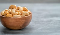 Fresh roasted cashew nuts in wooden bowl on gray concrete background, healthy raw organic snack for vegetarian nutrition and protein diet.