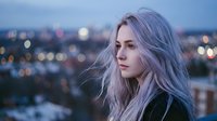 Young blonde woman with long wavy hair looking thoughtfully at city lights during blue hour twilight. Urban lifestyle portrait for marketing campaigns.