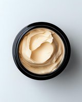 Luxurious beige face cream in black cosmetic jar photographed from above on white background, showing smooth texture and swirled pattern of moisturizer.