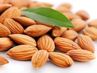 Fresh raw almonds with green leaf scattered on white background, macro view of nutritious nuts showing natural texture and detail for food photography.