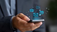 Glowing blue email icons floating above smartphone held by business professional in gray suit, depicting digital communication and mobile messaging technology.