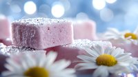 Pink marshmallow squares dusted with dark sprinkles arranged with fresh white daisies against soft blue bokeh background creating dreamy romantic mood for dessert photography.