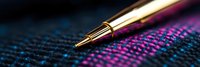 Gold metallic pen tip on textured denim fabric with vibrant pink and blue stitching pattern, macro photography showing fine detail and shallow depth of field.