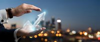 Businessman holding glowing upward arrow symbol representing growth, success, and financial progress against blurred city skyline at dusk for business concepts.