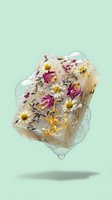 Frozen flowers in ice cube with colorful petals and herbs suspended in clear ice block floating against mint green background for natural skincare concepts.