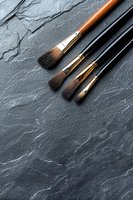 Professional artist paintbrushes with wooden and black handles arranged on textured slate background for art and craft projects.