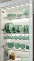 Organized kitchen cabinet with mint green dinnerware set featuring plates, bowls and cups on wire shelving racks for efficient storage and home organization.