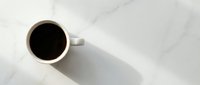 White coffee cup with black coffee on marble surface from above creating minimalist morning beverage scene for cafe branding and lifestyle content.