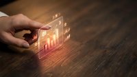 Businessman hand holding transparent smartphone displaying glowing financial charts and growth graphs for business analytics and investment strategy.