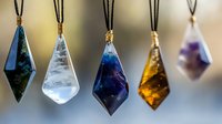 Collection of colorful crystal pendant necklaces hanging on dark cords featuring geometric diamond shapes in blue, clear, amber and purple stones.