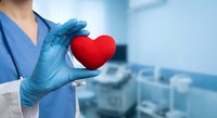 Healthcare professional in blue medical scrubs holding red heart symbol representing cardiology care and medical compassion in modern hospital setting.