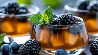 Fresh blackberry jelly dessert garnished with mint leaves and berries in glass bowls on dark background, selective focus on foreground.