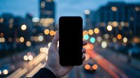 Hand holding blank smartphone screen against blurred city lights at dusk. Urban technology concept with bokeh background for mobile app mockups.