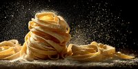 Fresh homemade pasta nests with flour dust against dark background, showcasing Italian cuisine craftsmanship for food photography.