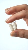 Hand holding two clear capsules with beige powder supplement on white background isolated for healthcare and wellness design.