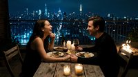 Romantic couple enjoying intimate dinner date on rooftop terrace with city skyline view at night, candlelit table setting for two with wine glasses and gourmet meal.