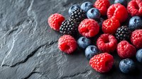 Fresh ripe raspberries, blackberries and blueberries scattered on dark stone background. Natural organic berries with vibrant colors for healthy eating.