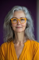 Confident mature woman with silver gray hair wearing bright yellow dress and orange glasses against purple background, natural aging concept portrait.