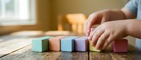 Child hands playing with colorful wooden building blocks on rustic table in bright natural light creating educational learning environment.