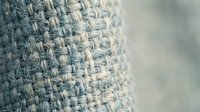 Close-up macro shot of natural burlap fabric texture showing detailed woven fibers and threads in neutral beige tones with soft blurred background.