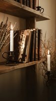 Rustic wooden shelves with vintage books, burning candles in metal holders, and dried lavender branches creating cozy farmhouse interior atmosphere.