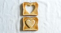 Golden toasted bread slices with heart-shaped cutouts on white fabric background. Creative breakfast concept for romantic morning meal preparation.