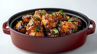 Glazed chicken wings with sesame seeds and green onions in burgundy ceramic baking dish. Sticky Asian-style sauce creates appetizing gloss on crispy wings.
