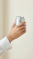 Hand holding silver aluminum can with pearl bracelet against neutral beige background for beverage marketing and product presentation.