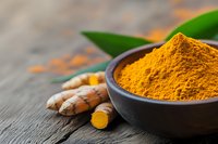 Fresh turmeric powder in bowl with raw turmeric roots on wooden background for cooking and natural health remedies.