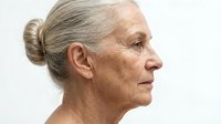 Senior woman with gray hair in bun, profile view, mature skin texture, aging skincare and dermatology concepts, isolated on white background.