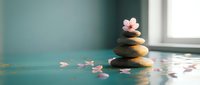 Zen spa stones balanced in pyramid with delicate pink cherry blossoms on turquoise surface near window creating peaceful meditation atmosphere.