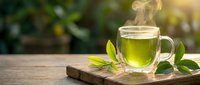 Steaming hot green tea in transparent glass mug on wooden board with fresh leaves, natural outdoor background for wellness and relaxation concepts.