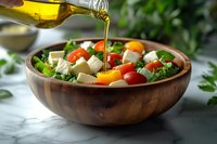 Fresh Greek salad with feta cheese, tomatoes and greens in wooden bowl being drizzled with golden olive oil for healthy Mediterranean cuisine.