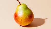 Fresh ripe pear with red and yellow gradient coloring on beige background with natural shadow, close up view of whole fruit with stem.